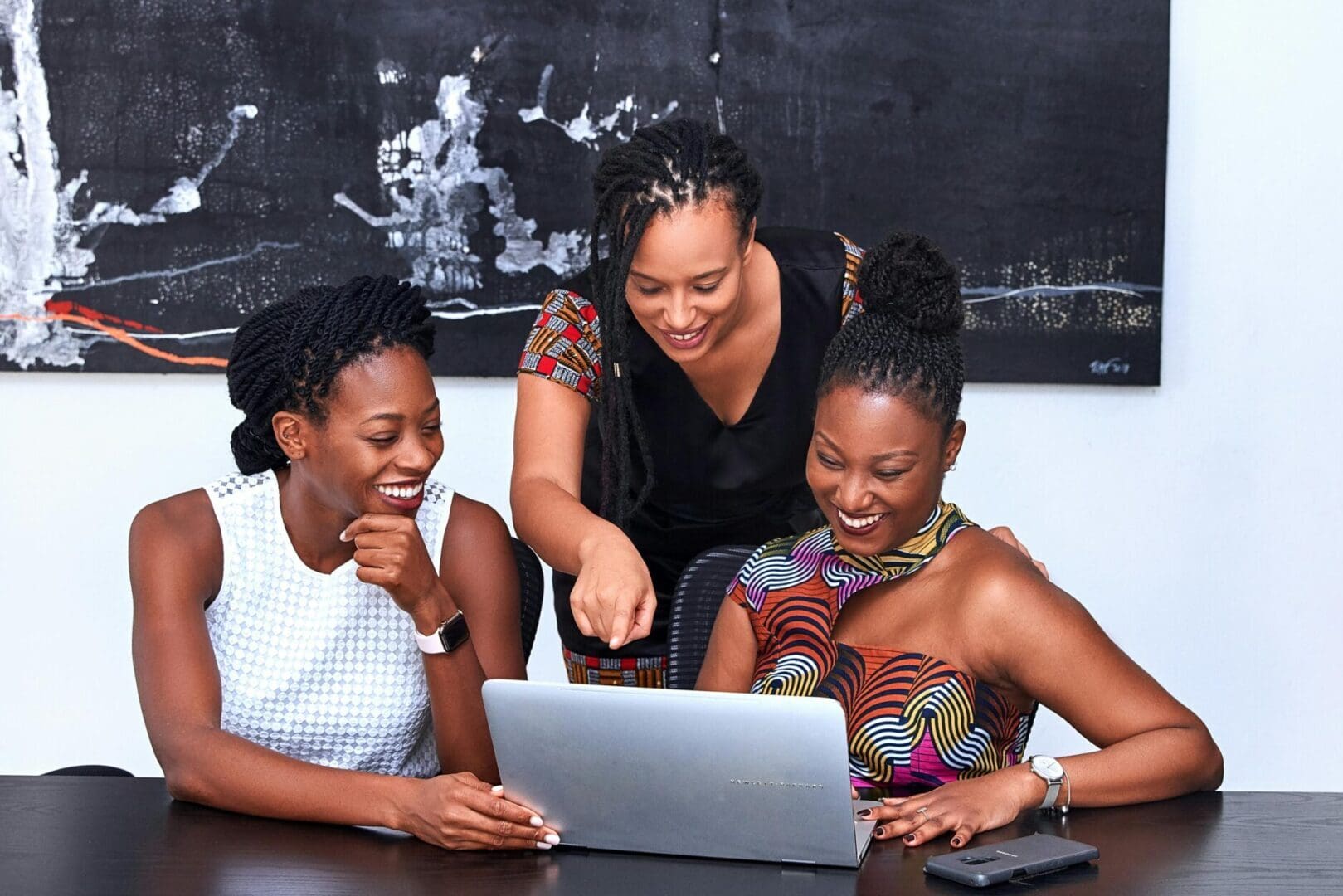 Three women are sitting at a table looking at the laptop.