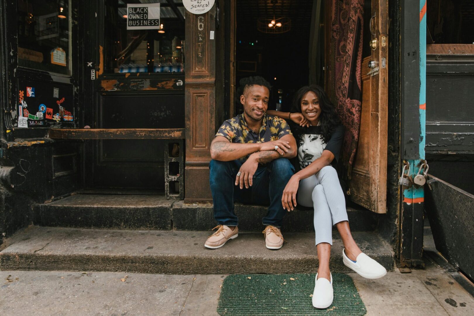 A man and woman sitting on the steps of a store.
